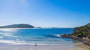 Ein Strand mit klarem, blauem Wasser, einem Sandufer und einem entfernten Berg.