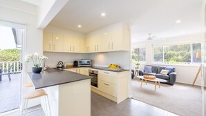 Eine moderne Küche mit Kochinsel, ein Essbereich mit Sofa und Couchtisch sowie ein Balkon mit Sitzgelegenheit.