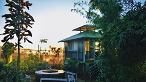 A rustic cabin with a wooden exterior, a circular fire pit, and a staircase leading to a covered porch. - Forrest Homestay Villa (Bhor)