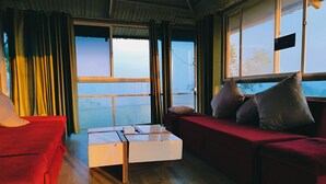 A room with a red sofa, a white coffee table, and a view of the outdoors through large windows. - Forrest Homestay Villa (Bhor)