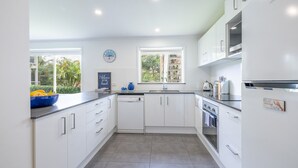 A modern kitchen with white cabinets, a dishwasher, an oven, and a refrigerator. There is a window with a view of greenery outside.