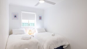 Een slaapkamer met twee bedden, een plafondventilator, een raam met uitzicht en twee kunstwerken aan de muur.