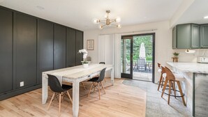 Eine moderne Küche mit dunklen Schränken, einer weißen Arbeitsplatte und einem Essbereich mit einem Holztisch und Stühlen.