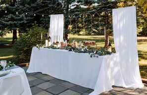 An outdoor event setup with a table covered in white cloth, decorated with greenery and candles, and string lights above. - Large Groups, Sleeps 12, Accessible , 5BR, Long Term Rental  (Bay City)