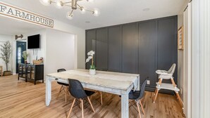 Ein Essbereich mit einem Holztisch, schwarzen Stühlen und einer weißen Orchideen-Dekoration. Eine dunkle Wand und eine Deckenleuchte sind sichtbar.