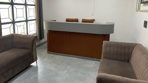 A reception area with a modern desk, two brown sofas, and a large window with a geometric pattern. - The Royal Inn (Faridabad)