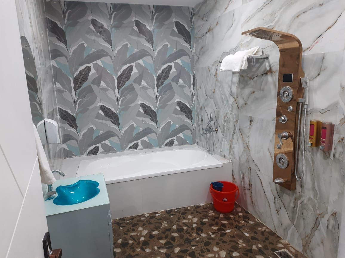 Une salle de bain avec un mur en marbre, une douche avec un panneau en bois, un lavabo bleu et un seau rouge.