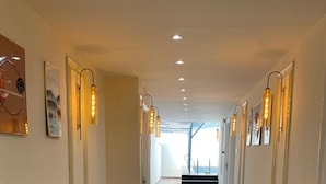 A hallway with wooden flooring, recessed ceiling lights, and wall-mounted light fixtures. - The Royal Inn (Faridabad)