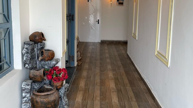 A hallway with wooden flooring, decorative stone planters, and wall-mounted lighting fixtures. - The Royal Inn (Faridabad)