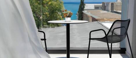 Un balcón con una mesa redonda y dos sillas, con vistas a un paisaje urbano y al mar.