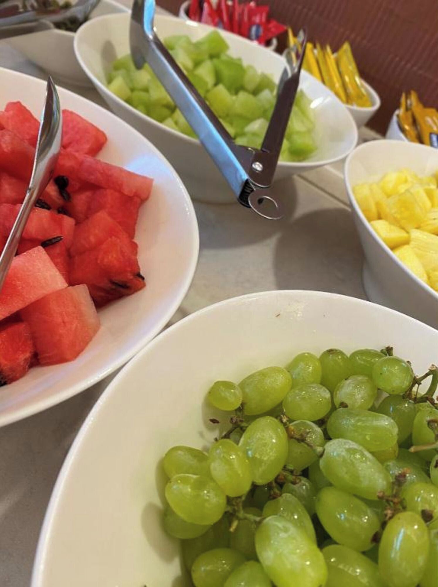 Una mesa con tazones de sandía, uvas y trozos de piña.