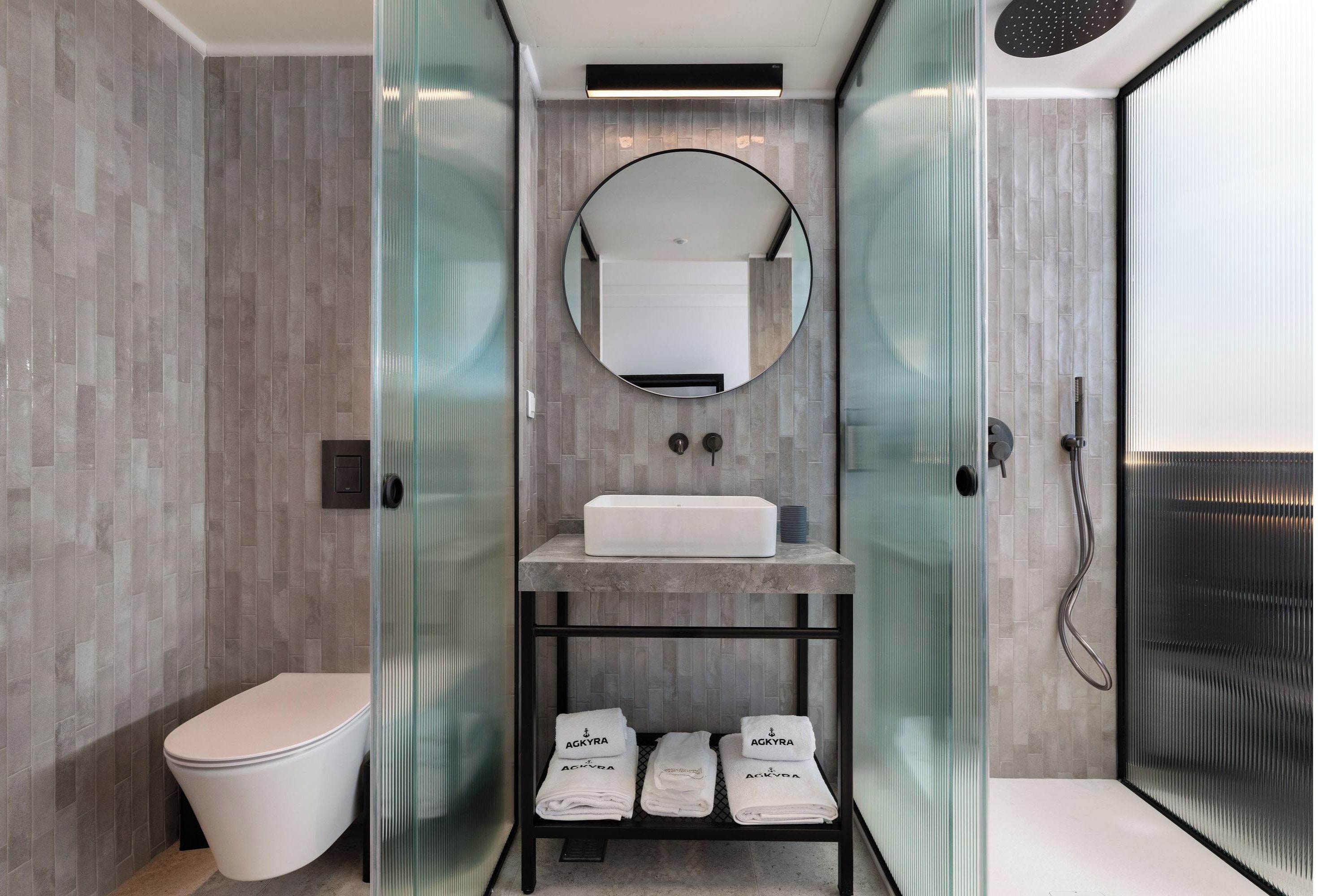 Een moderne badkamer met toilet, een wastafel op een plank, een spiegel en een douchehoek.