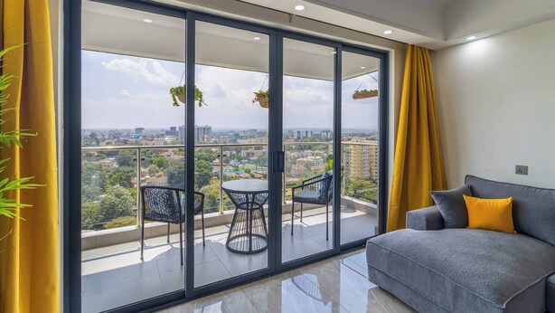 Ein Balkon mit Blick auf die Stadt, ein graues Sofa und gelbe Vorhänge.