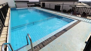 Ein rechteckiger Pool mit klarem, blauem Wasser, umgeben von einer gefliesten Terrasse und Metallgeländern.