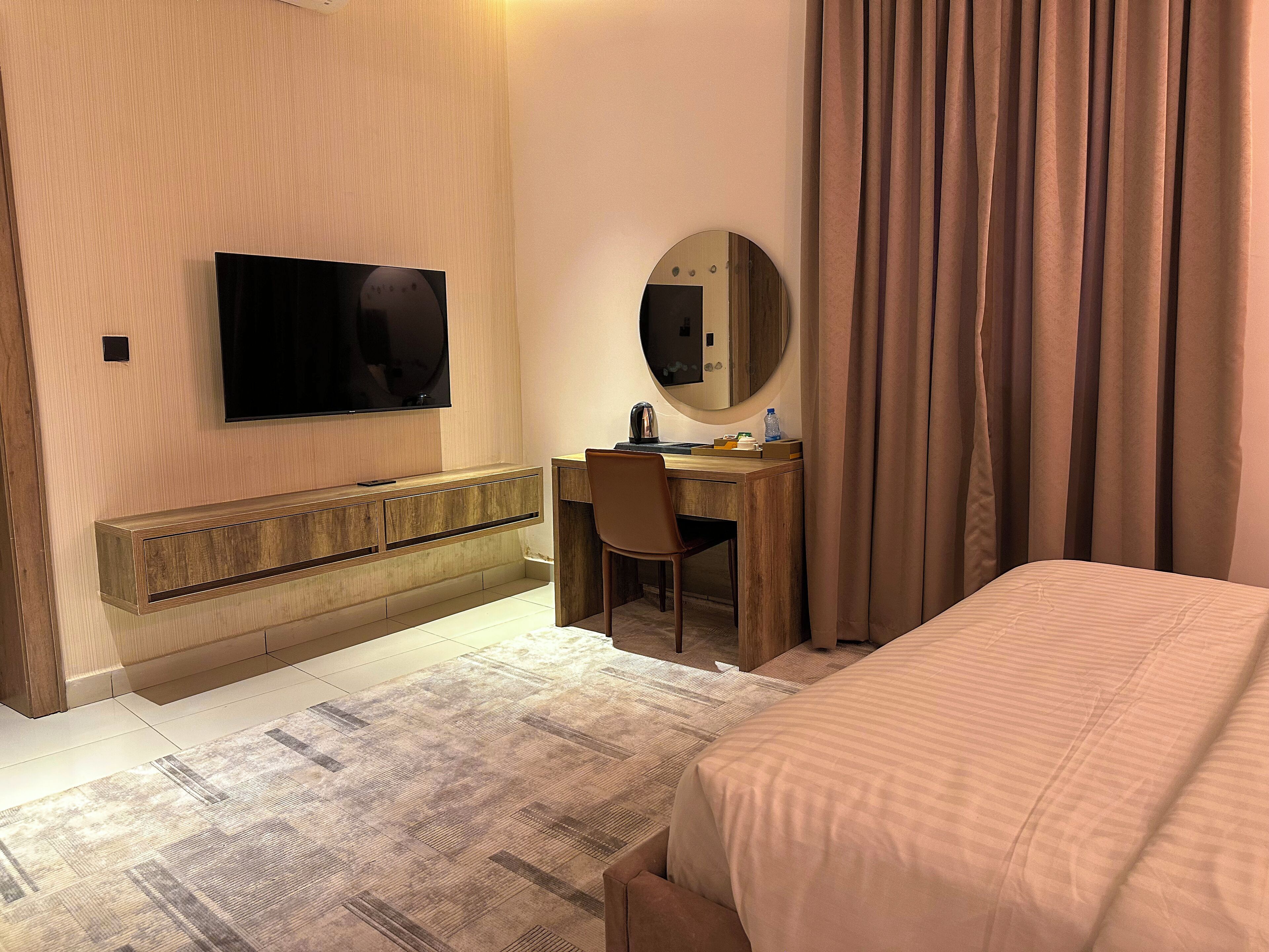 A hotel room with a bed, a desk, a chair, a television, a mirror, and a window with curtains.