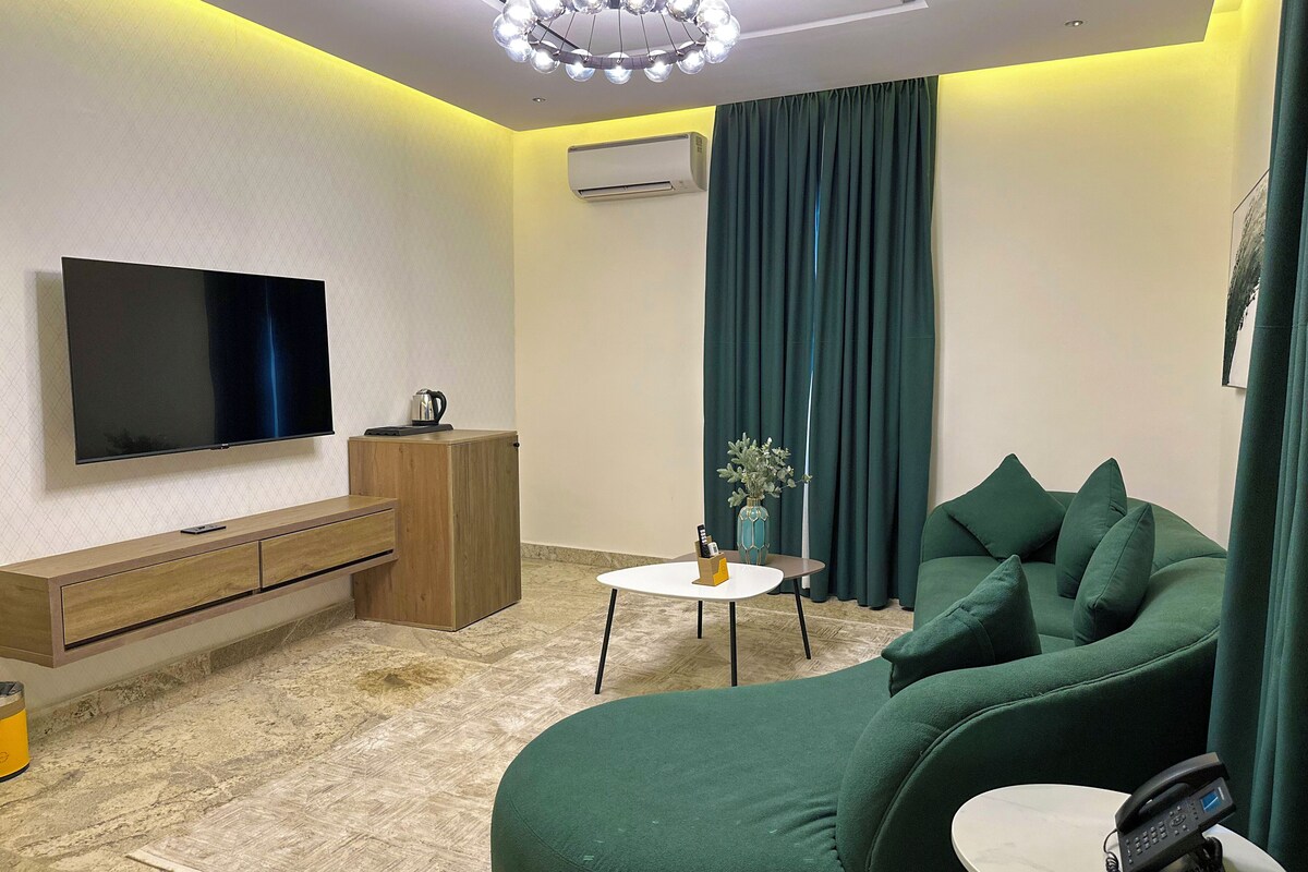 Un soggiorno moderno con televisore a schermo piatto, mobile TV in legno, divano verde, tavolino rotondo e telefono su un comodino.
