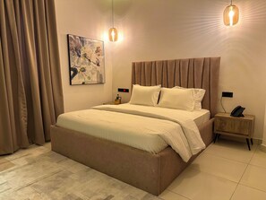 A modern hotel room with a large bed, a bedside table with a phone, and a painting on the wall. - ELYSIAN HOTEL  (Abuja)