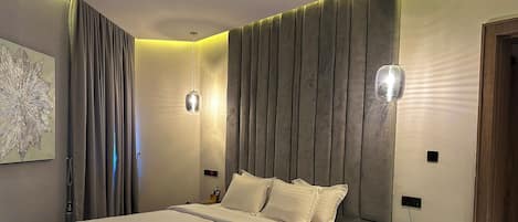 A modern hotel room with a large bed, a bedside table with a phone, and a wall-mounted light fixture.