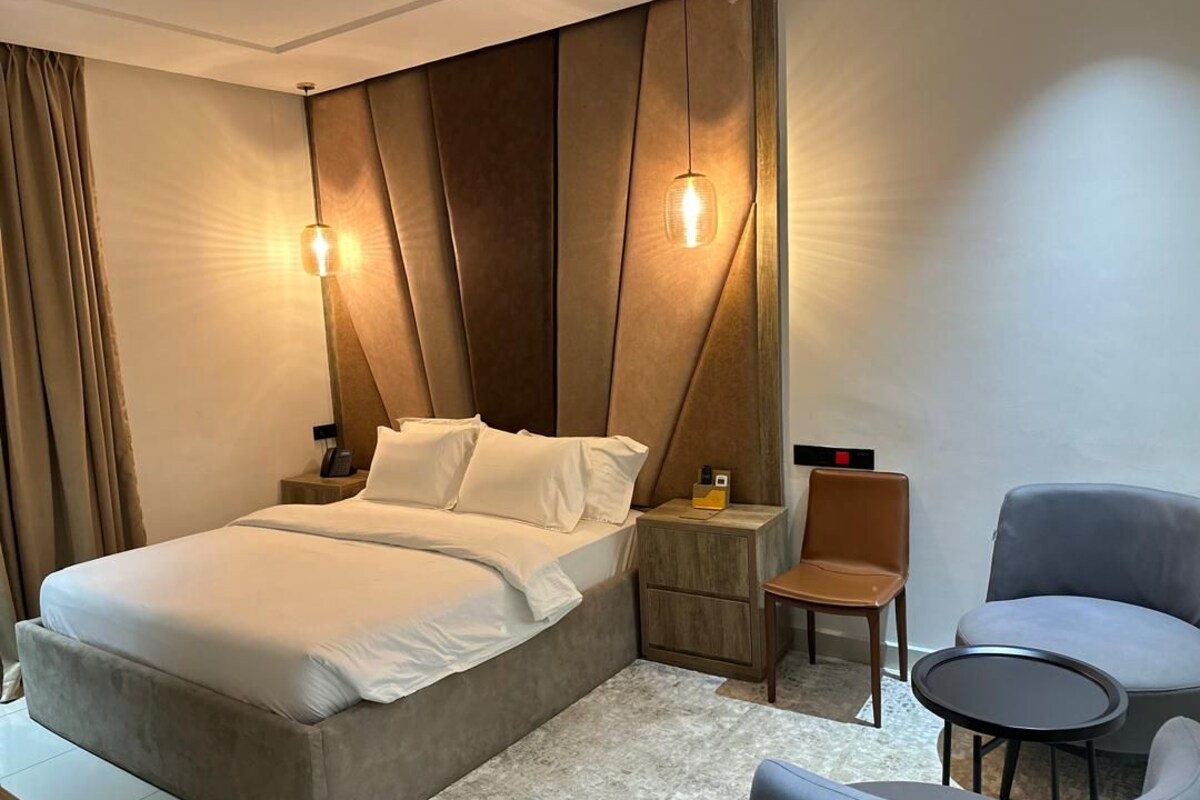 A modern hotel room with a large bed, a wooden nightstand, a chair, and a small table.