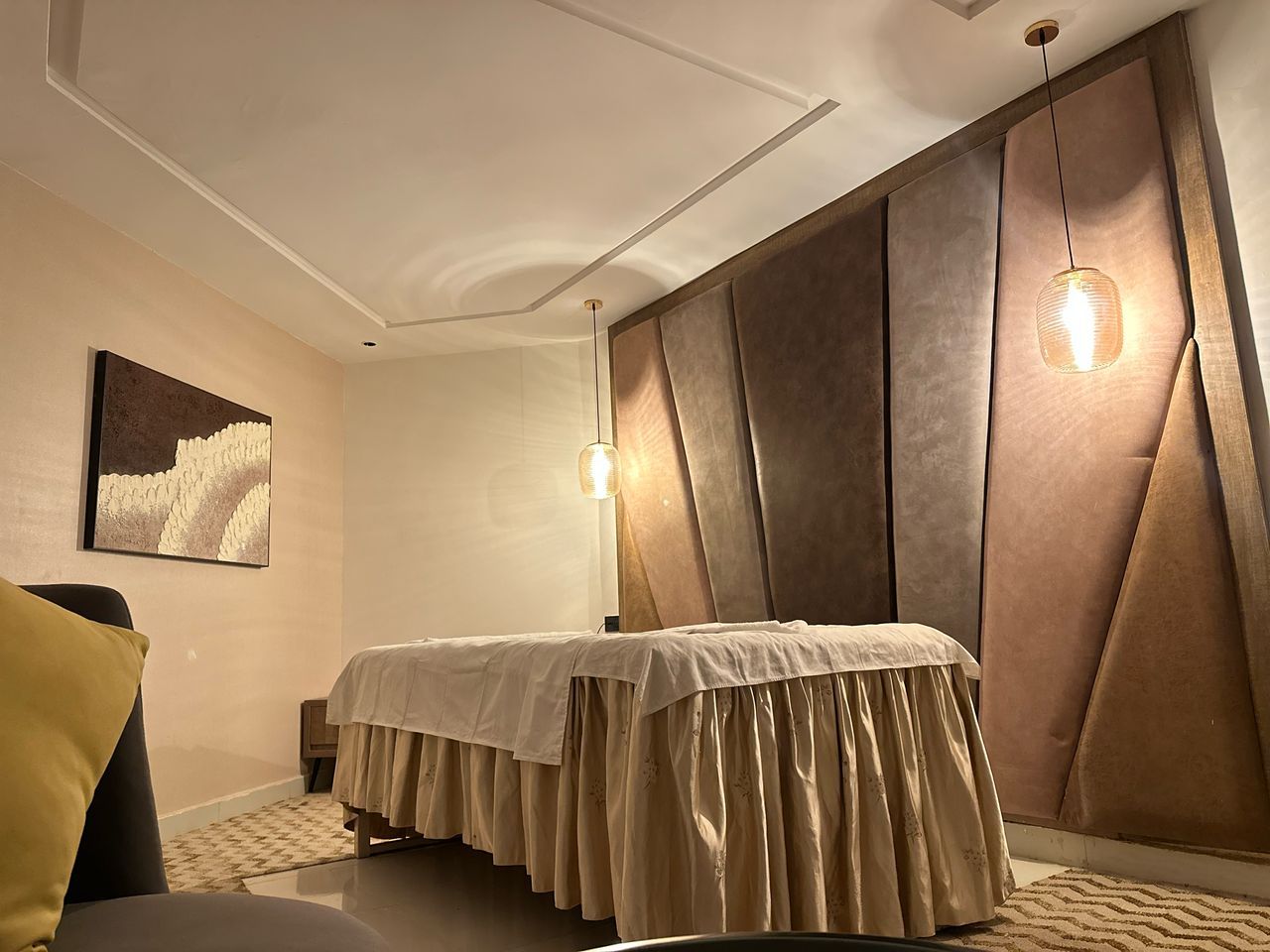A modern bedroom with a bed, a nightstand, a chair, and a wall-mounted light fixture.