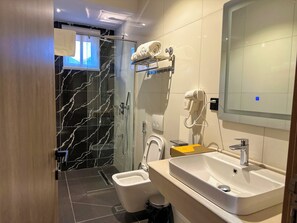 A modern bathroom with a glass shower enclosure, a white toilet, a sink with a mirror, and a towel rack with towels. - ELYSIAN HOTEL  (Abuja)
