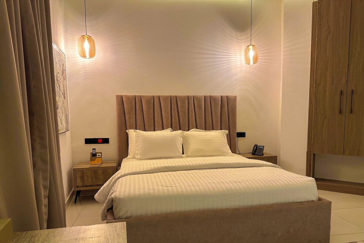 Una camera d'albergo con un letto grande, un comodino, un tavolino, un telefono e un armadio.