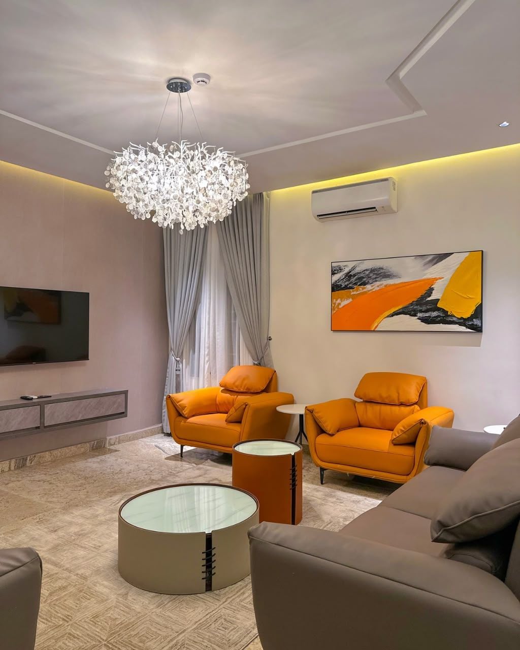 A modern living room with a chandelier, a flat-screen TV, and a painting on the wall.