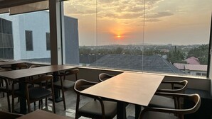 A restaurant with tables and chairs, large windows with a view of the cityscape and sunset. - ELYSIAN HOTEL  (Abuja)