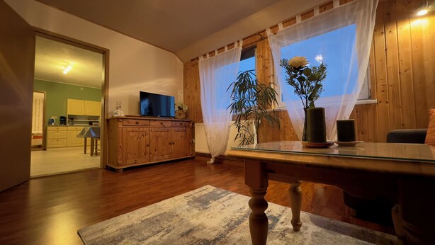 A living room with a wooden cabinet, a glass coffee table, a TV, and a potted plant. - Cozy vacation apartment in an idyllic natural location (Rosenthal-Bielatal)