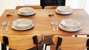 A dining table set with four plates and cutlery, surrounded by wooden chairs.