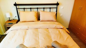 A neatly made bed with beige linens and two rolled towels.