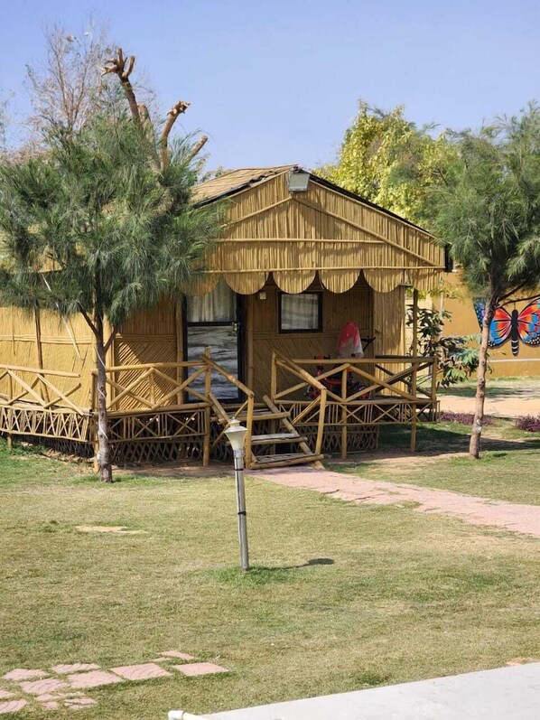 A rustic wooden building with a thatched roof, surrounded by a bamboo fence and small trees. - Altara Resort (Jaipur)