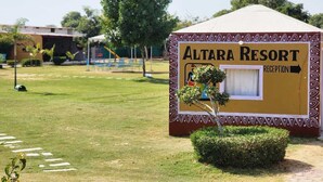 A reception area for Altara Resort with a clear pathway leading to it, surrounded by greenery and a playground in the background. - Altara Resort (Jaipur)
