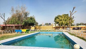 A rectangular swimming pool with a tiled edge, surrounded by a white fence, and a small white structure with a spherical top. - Altara Resort (Jaipur)