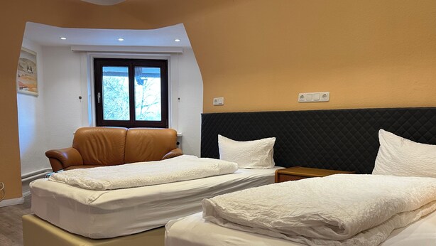 A hotel room with two beds, a brown leather chair, a window with a view of trees, and a black headboard. - Your haven of peace near Hamburg Airport (Quickborn)