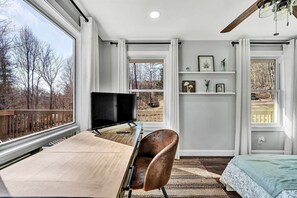 A bedroom with a desk, a chair, a bed, a TV, and large windows with a view of trees. - Peaceful 3BR Escape With National Forest Access (Fincastle)