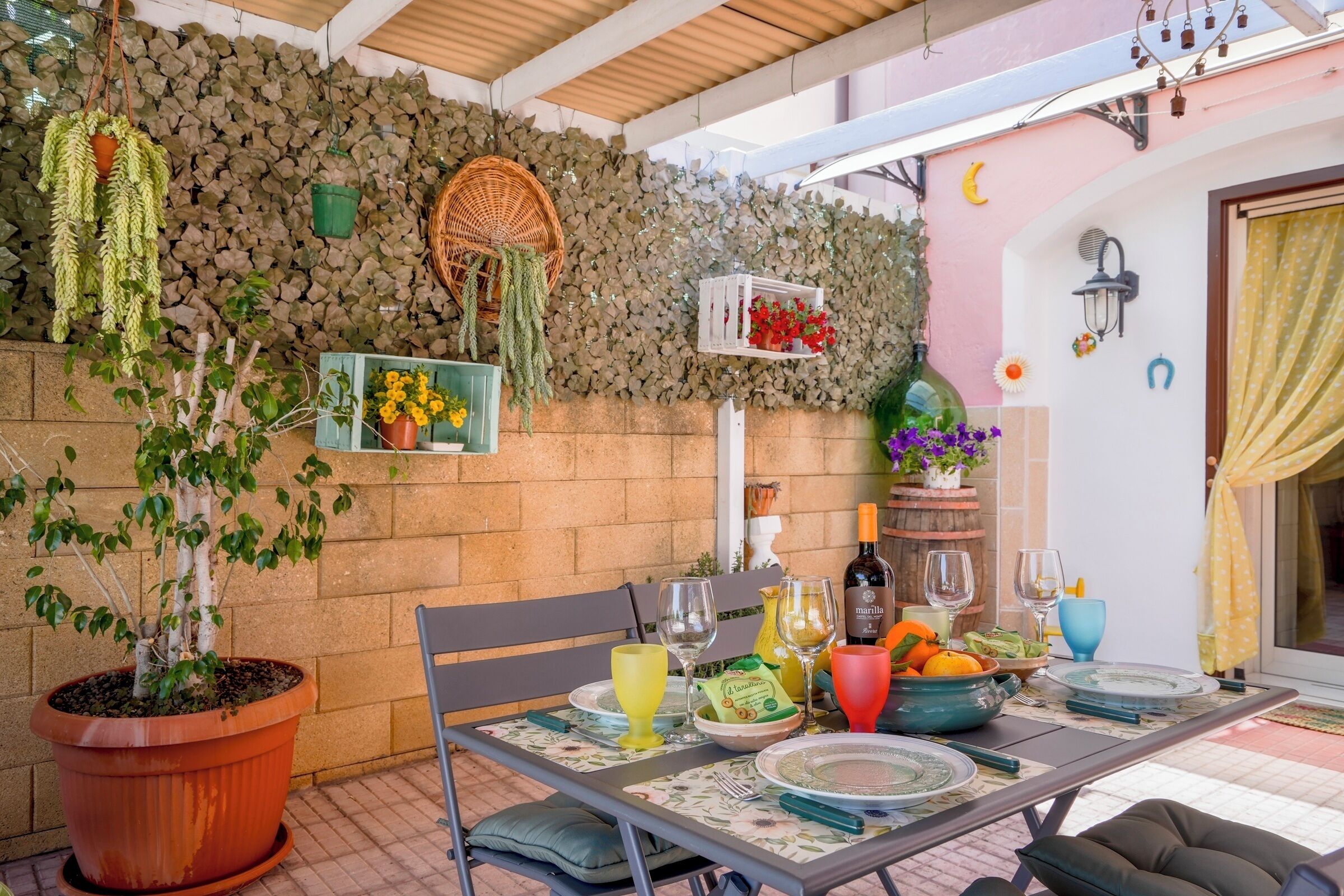 Un patio techado con una mesa dispuesta para comer, rodeado de plantas en macetas y adornos colgantes.