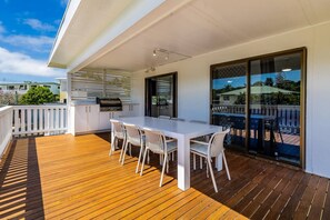 A covered outdoor dining area with a wooden deck, a white table, and chairs. - A Lure - 100m to Main Beach! (Agnes Water)