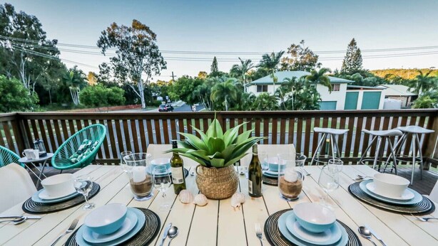 A dining table set outdoors with chairs, a potted plant, and a view of houses and trees. - A Lure - 100m to Main Beach! (Agnes Water)