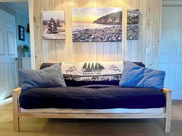 A wooden sofa with a dark blue cover, a decorative pillow, and a blanket with maritime illustrations.