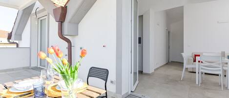 Ein moderner, offener Wohnbereich mit Essplatz, der einen Holztisch und Stühle, eine Glasvase mit Blumen sowie einen Blick in den angrenzenden Raum bietet.