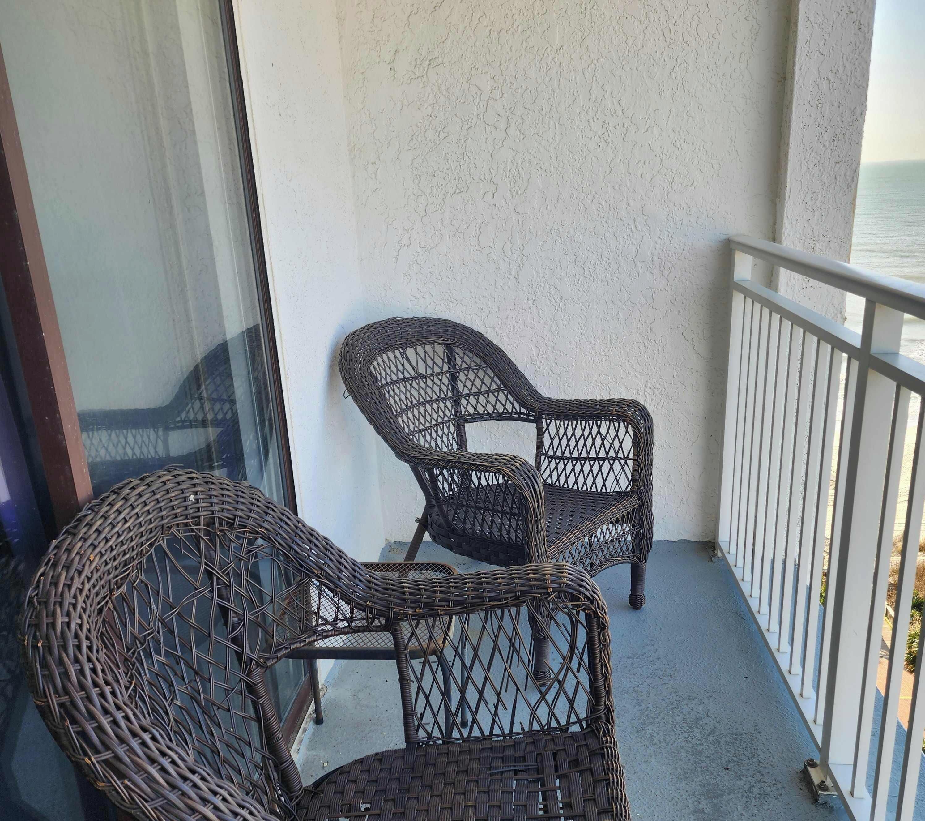 Un balcon avec deux fauteuils en osier, une balustrade blanche et une vue sur la mer.