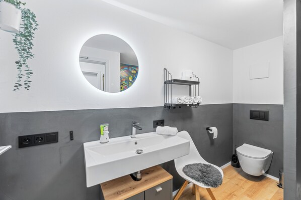 Un baño moderno con un lavamanos blanco, un espejo redondo y un inodoro.