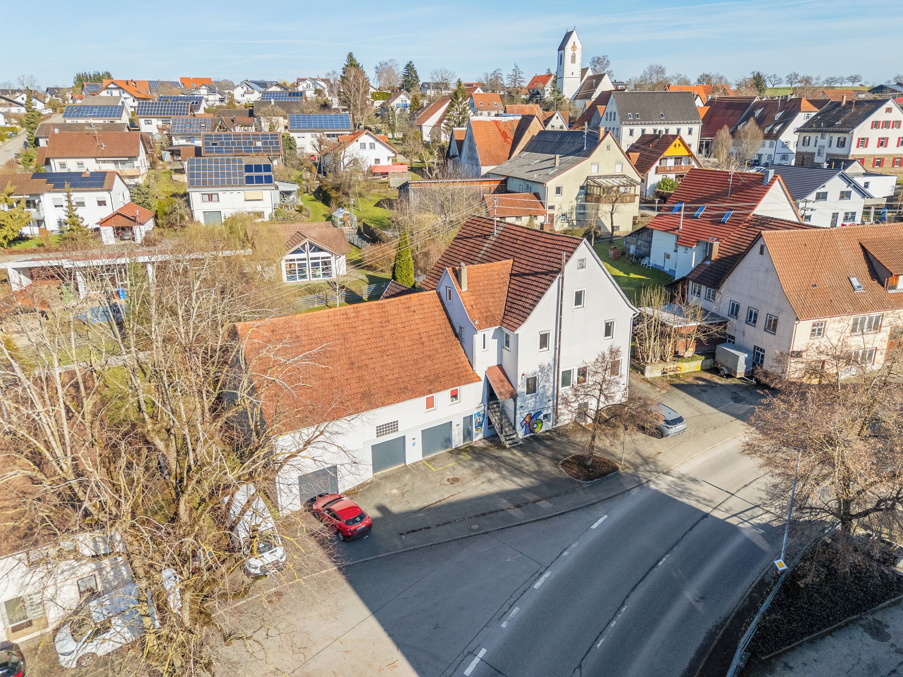 Eine Vogelperspektive eines Wohngebiets mit Häusern, einer Kirche und einem roten Auto, das an der Straße geparkt ist.