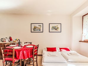 A room with a dining table set for two, a bed with white linens, and two framed pictures on the wall.