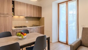 Moderni keittiö, jossa on puiset kaapit, kaasuliesi ja pesuallas. Keittiössä on ruokapöytä tuoleineen sekä kulho täynnä hedelmiä.