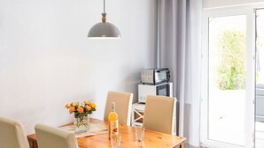 Un comedor con una mesa de madera, cuatro sillas, un jarrón con flores, una botella y un vaso. Hay un microondas en un estante detrás de la mesa.