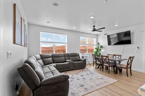 A modern living room with a sectional sofa, dining table, chairs, and a TV mounted on the wall. - Zion Cliffside Retreat l Gem for Relaxation (Hurricane)