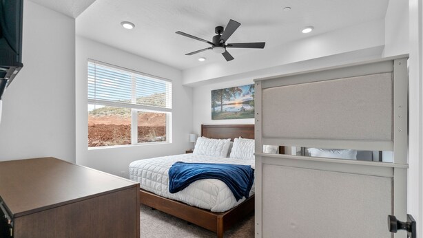 Une chambre à coucher avec un lit, un ventilateur de plafond, une fenêtre avec des stores, un tableau au mur et une armoire.