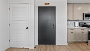 Une cuisine moderne avec un plancher en bois clair, des armoires blanches, un four à micro-ondes en acier inoxydable et un panneau de signalisation indiquant la sortie au-dessus d’une porte sombre.